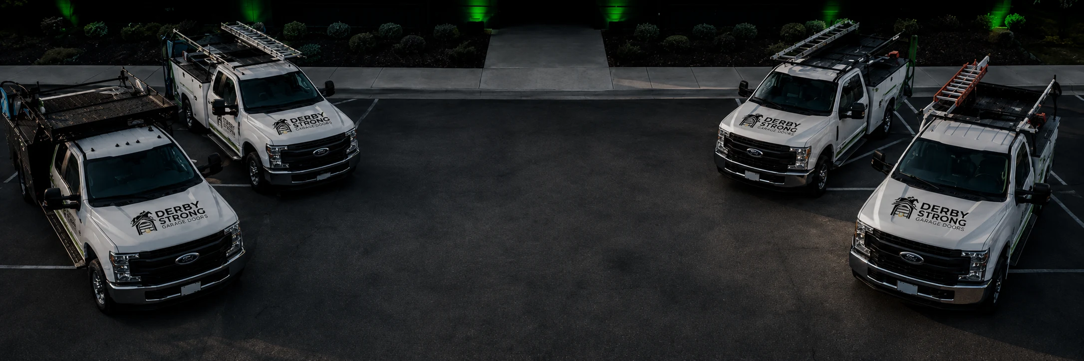 Four Derby Strong Garage Doors service trucks parked outside at night