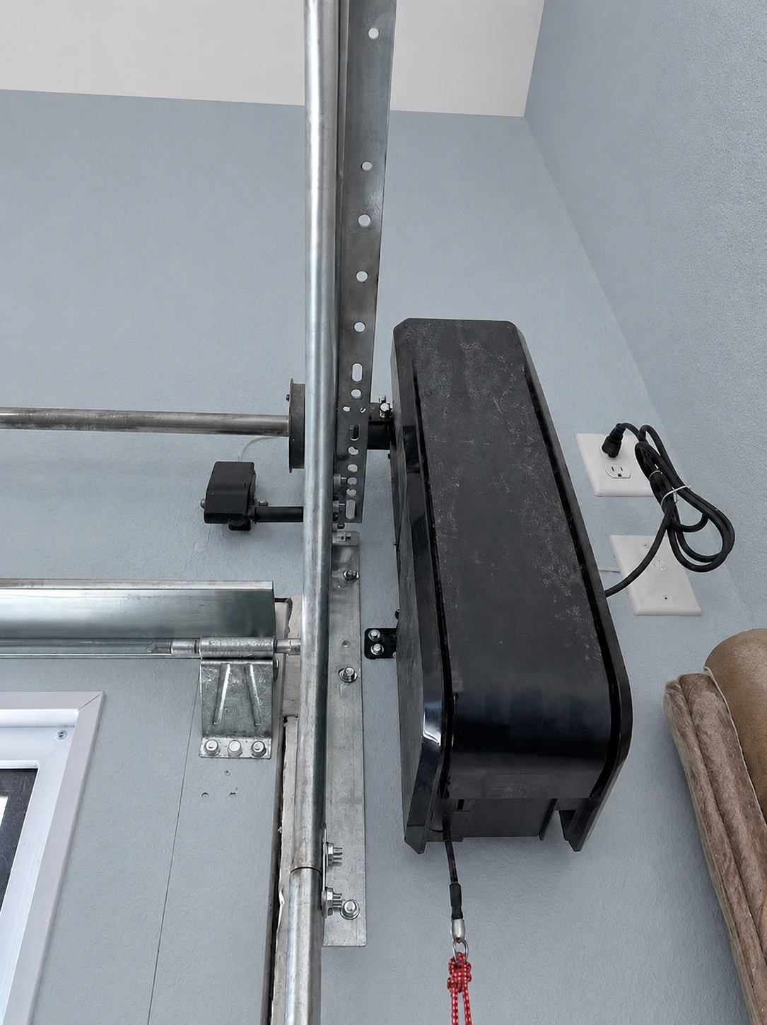 Side-mounted opener beside a torsion shaft against a blue-gray wall